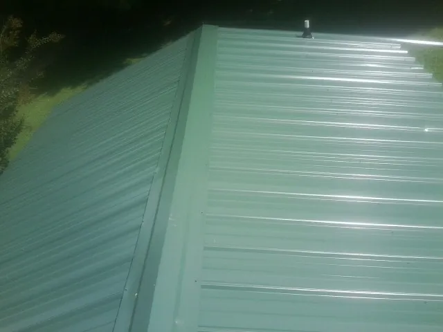 New green metal panels meeting at the ridge of a roof — Flat Roof Repair work by our crew in Barrington