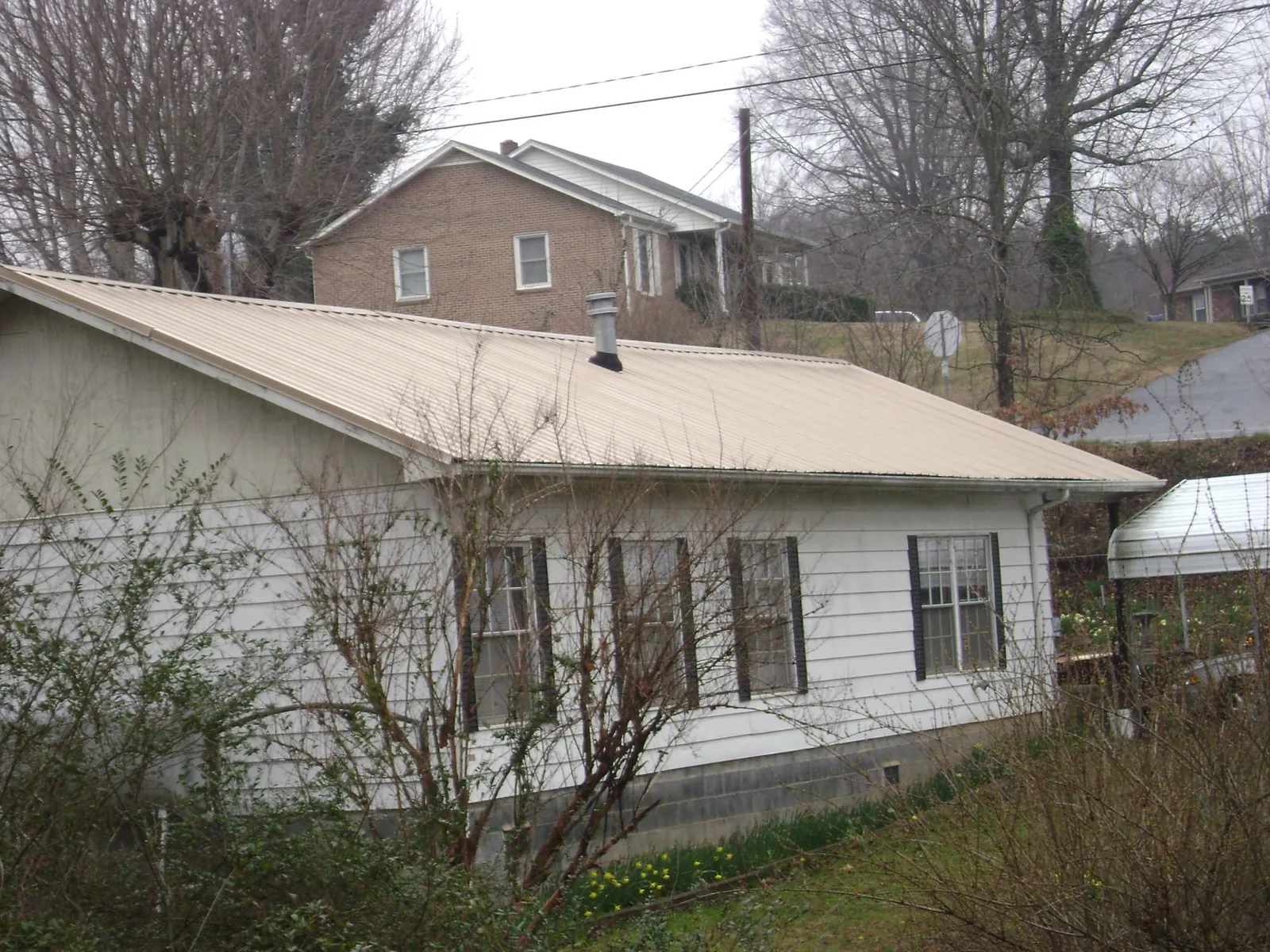 Tan metal roof on a white sided house set into a hillside — Commercial Roofing by Roofing Brothers in Barrington